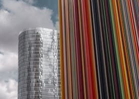 Un gratte-ciel moderne jouxte une œuvre d'art à rayures verticales colorées sur fond de ciel nuageux.