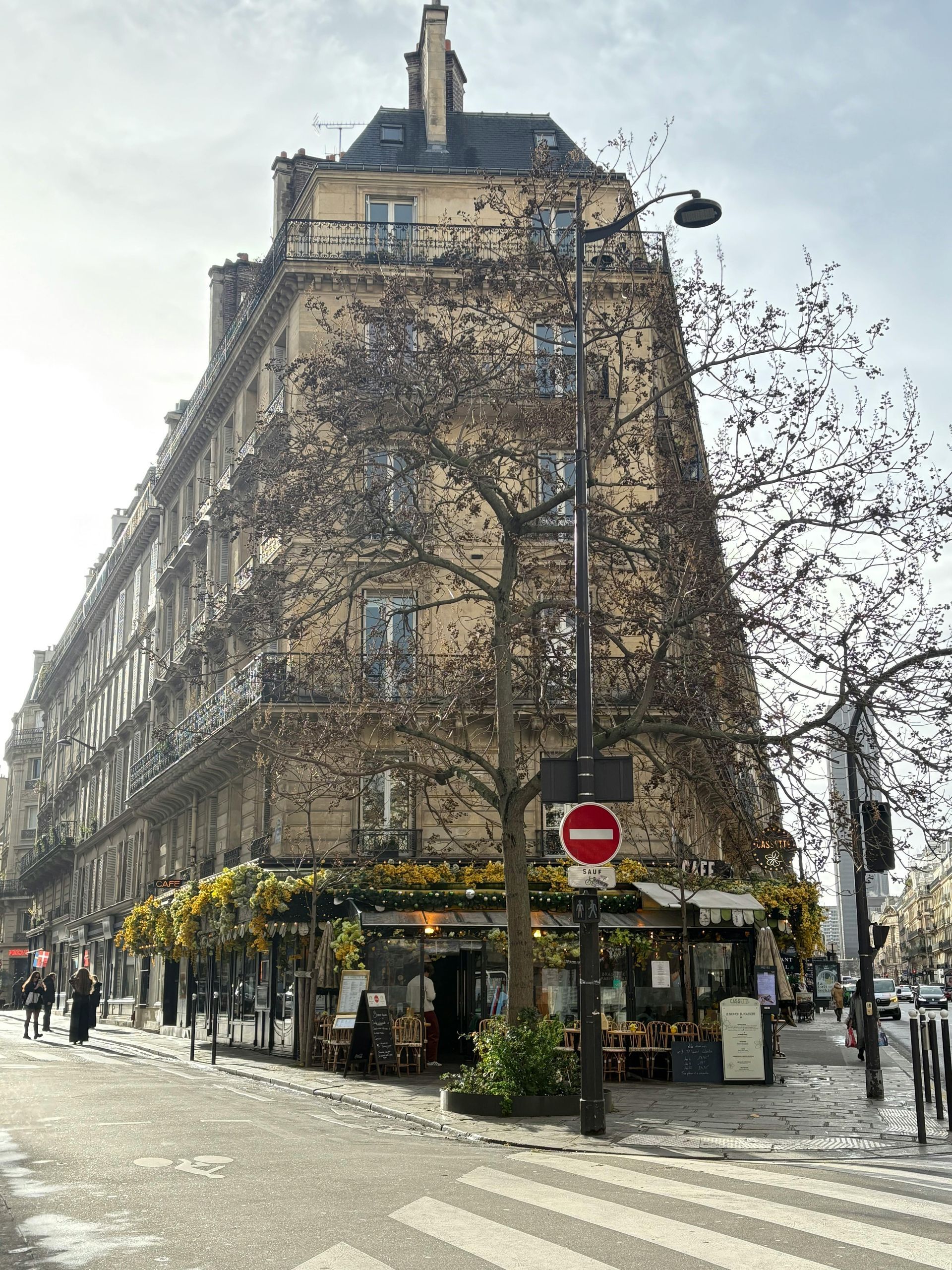 Immeuble d'angle à Paris avec un restaurant ; arbre devant et panneau « Sens interdit ».