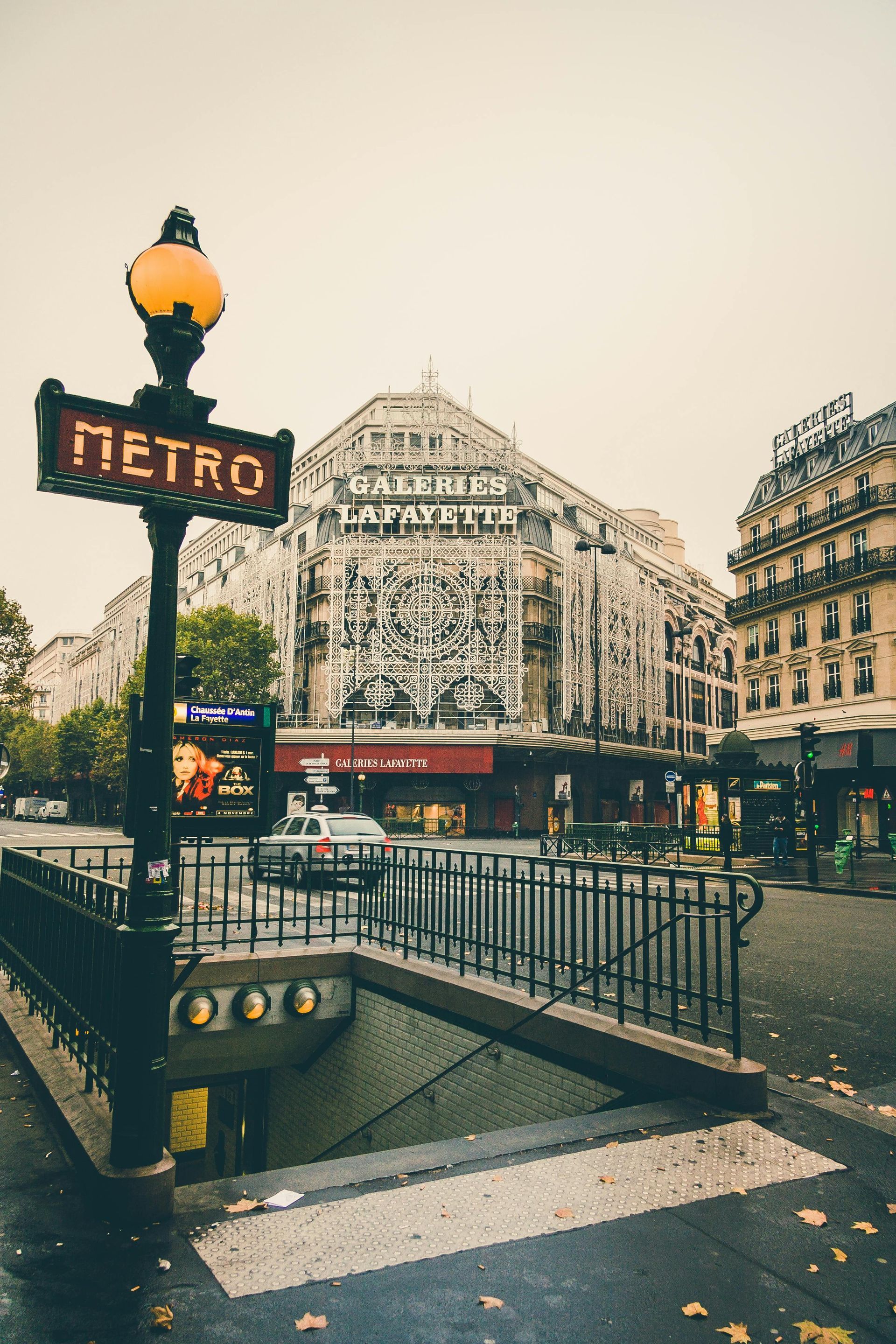 Entrée du métro parisien avec le panneau « Métro » devant un grand magasin. Jour de pluie.
