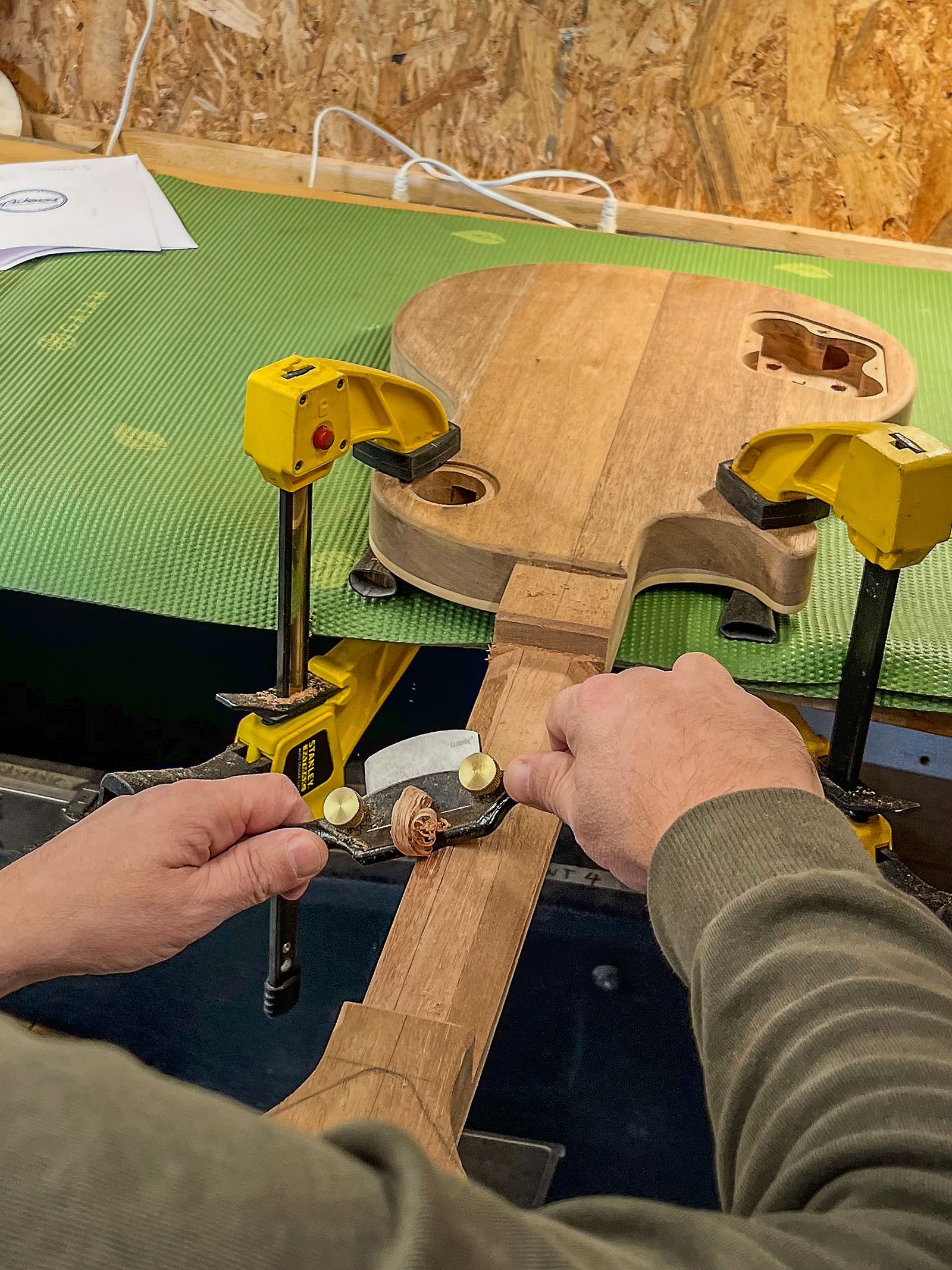 Iemand werkt in een werkplaats aan een gitaar. Gitaar nek shaping. Handgemaakte gitaar.  Art of Noise Guitars