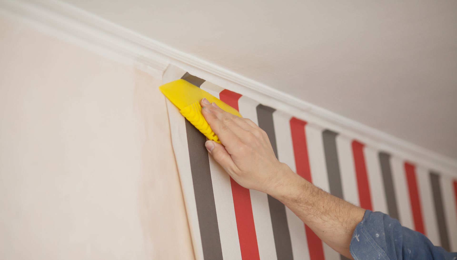 Person Smoothing Wallpaper Against a Wall Near a Ceiling Trim — G.N Painting and Decorating in Port Macquarie, NSW