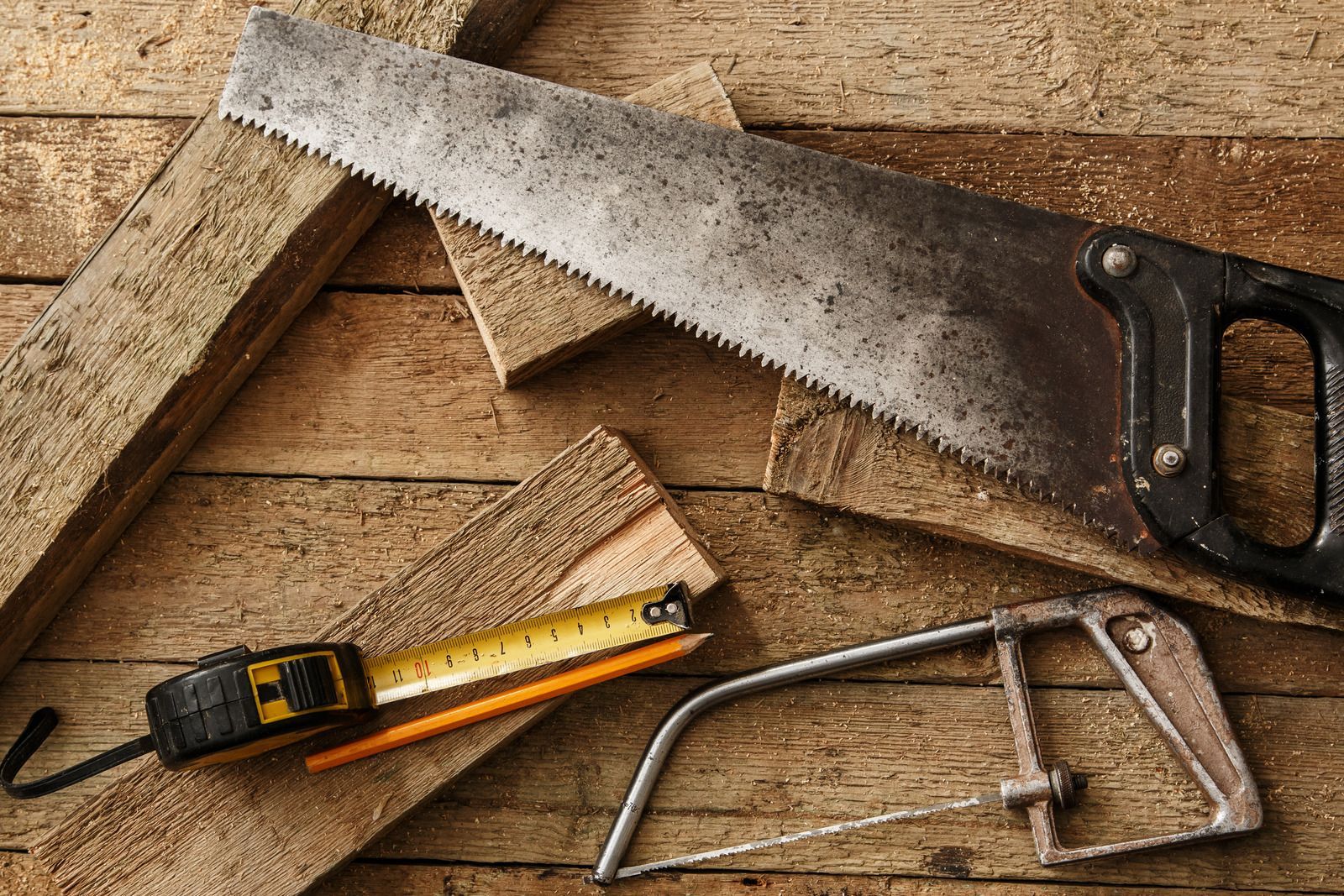 A saw , tape measure , and pencil are on a wooden table.