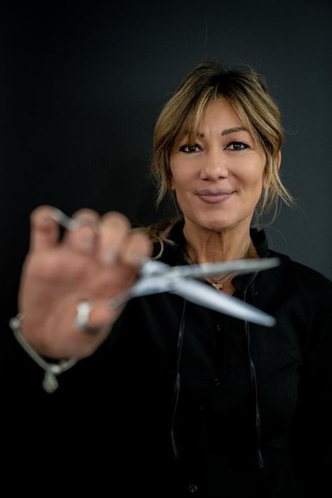 Donna sorridente, con forbici aperte, ambiente professionale con luci soffuse.