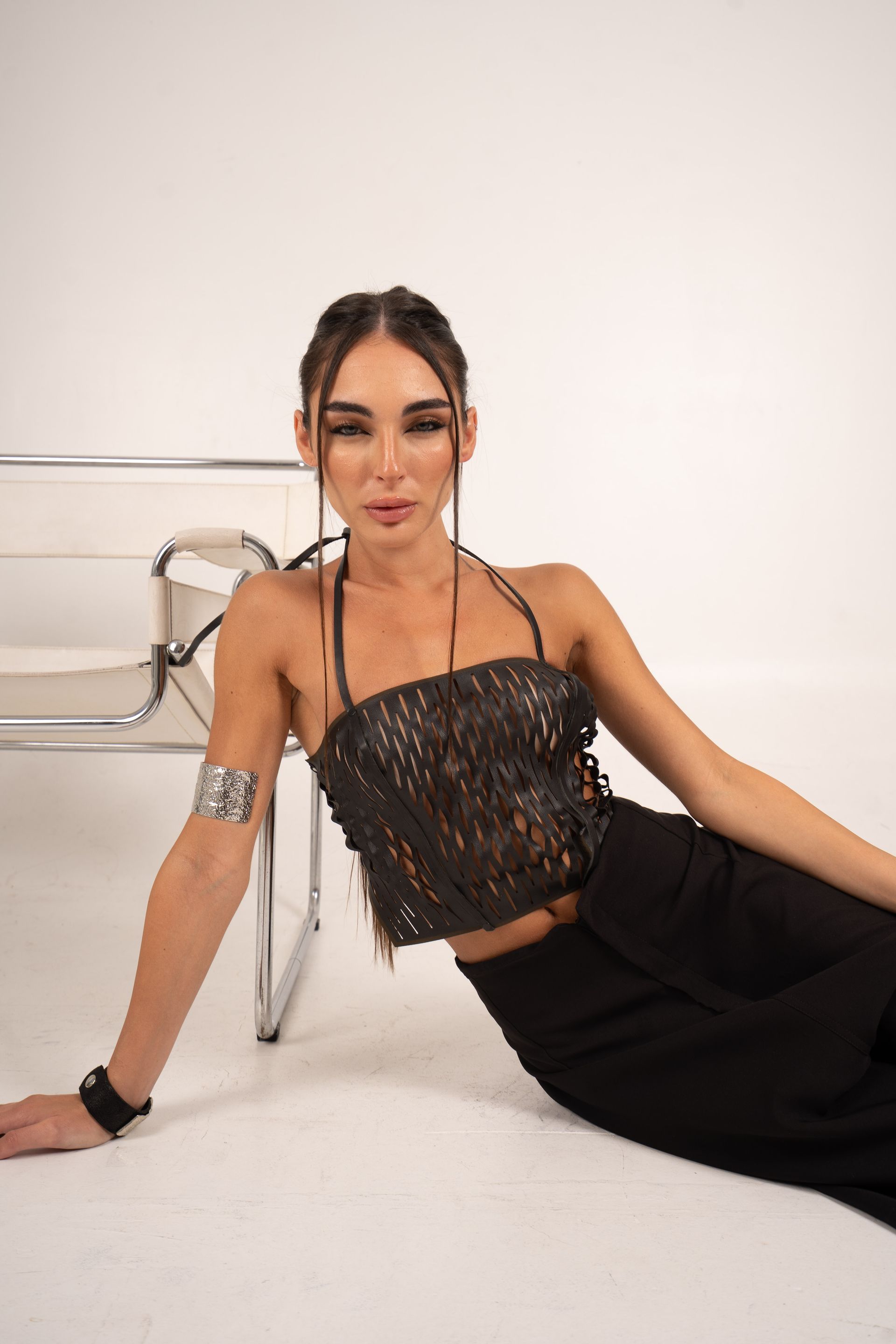 Mujer con top y pantalones de encaje negro, sentada cerca de una silla.