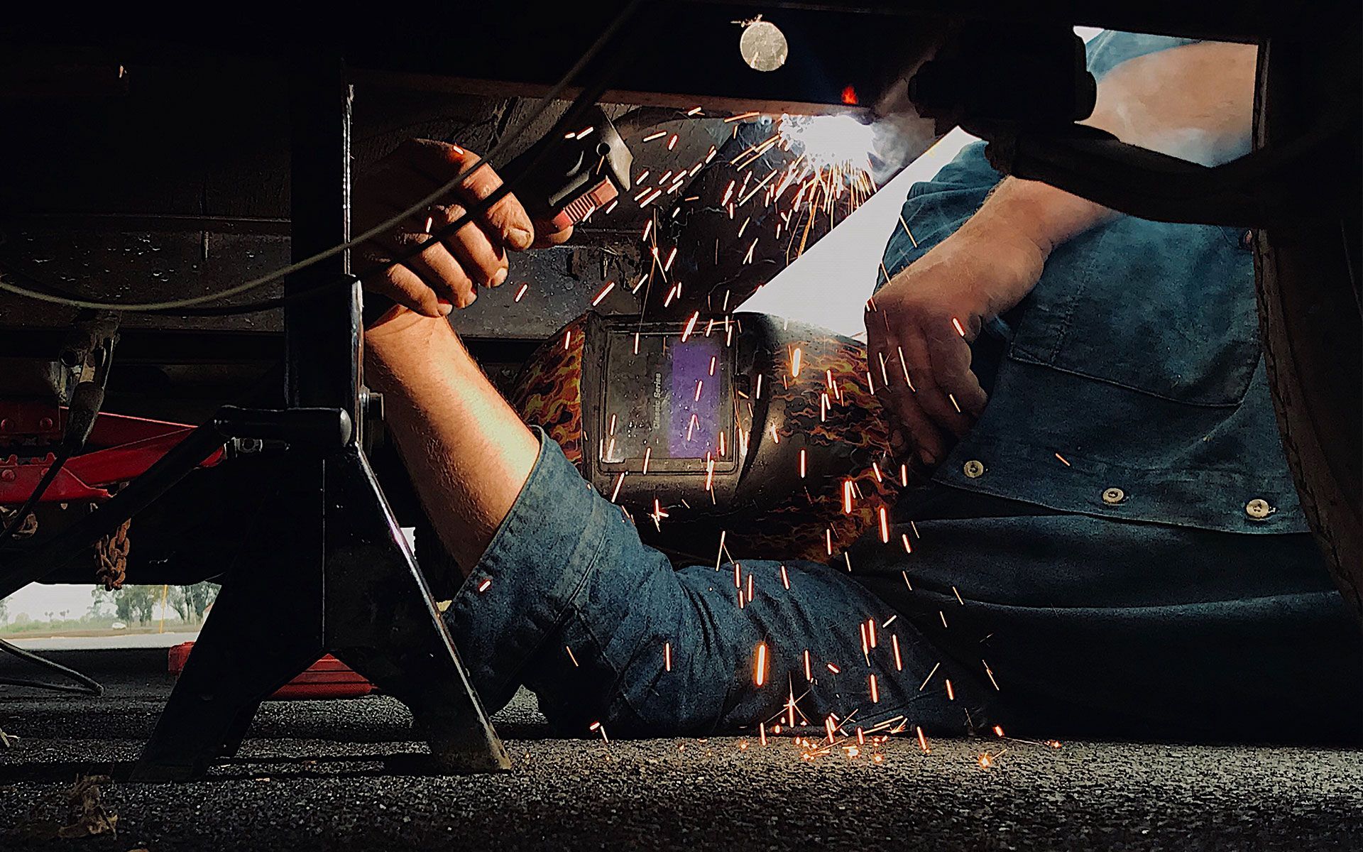 A man is welding a piece of metal under a car.