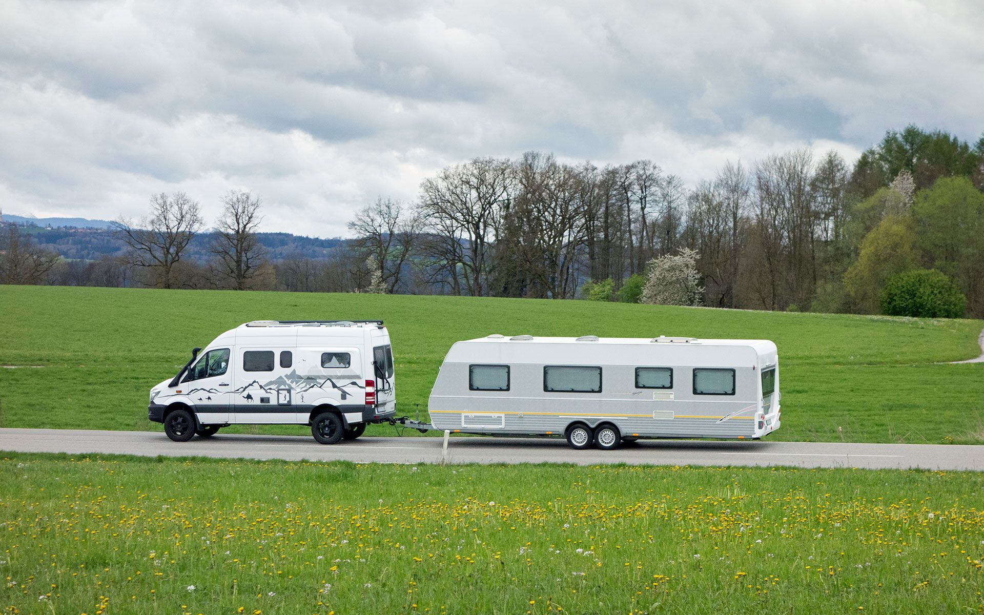 A white van is pulling a trailer down a road.