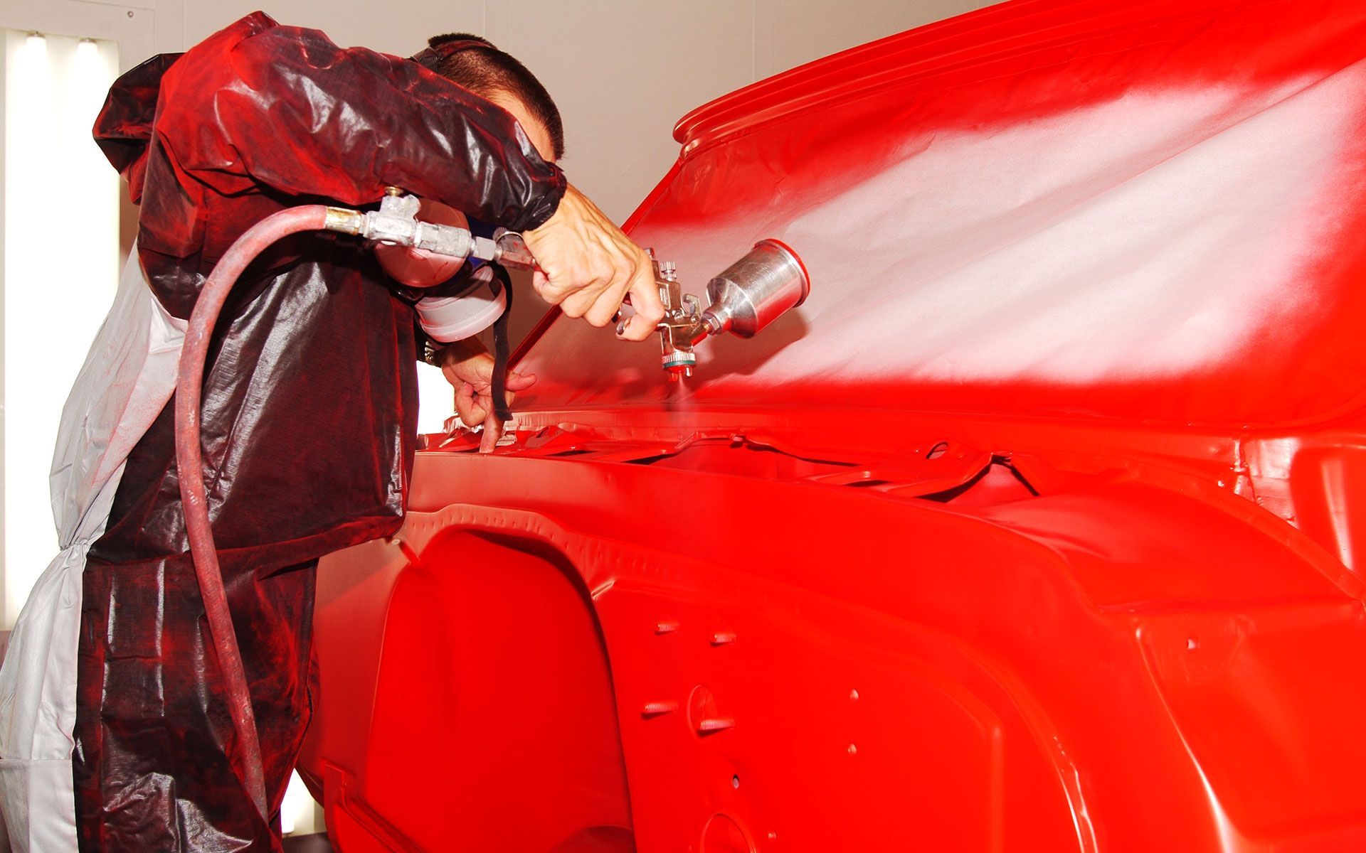 A man is spray painting a red car in a garage.