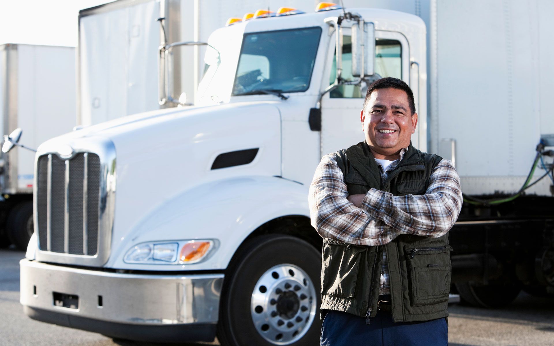A man is standing in front of a semi truck with his arms crossed.