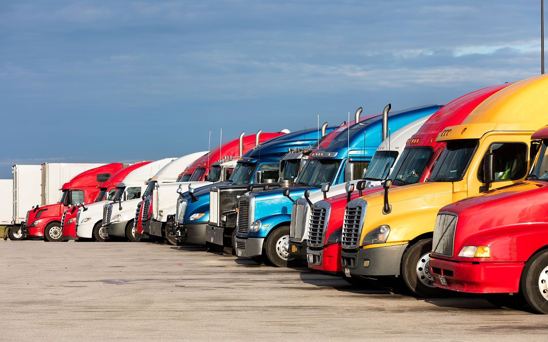 A row of semi trucks are parked in a parking lot.