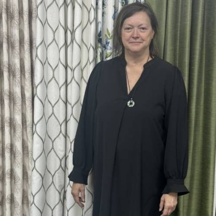 Woman in black dress stands near patterned curtains.