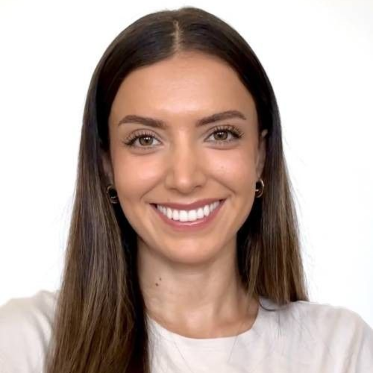 Woman with brown hair, smiling, wearing a light-colored top, in front of a white background.