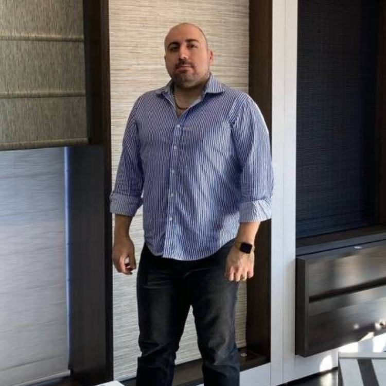 Man in blue striped shirt and black pants, standing indoors, arms at sides, watch on wrist.