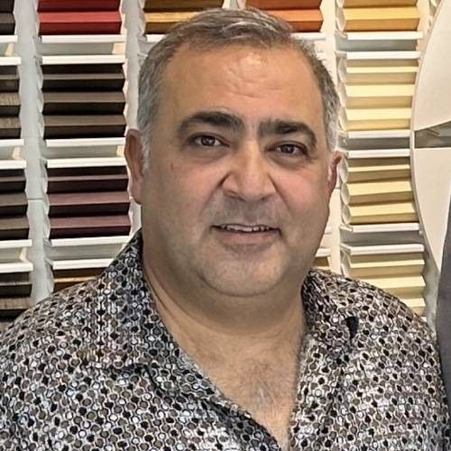 Man in patterned shirt smiles, standing in a shop with frame samples.