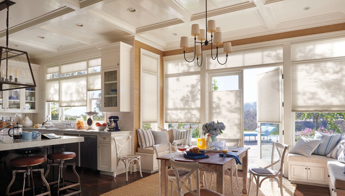 Bright kitchen with white cabinets, beige blinds, and a dining table set near a window.