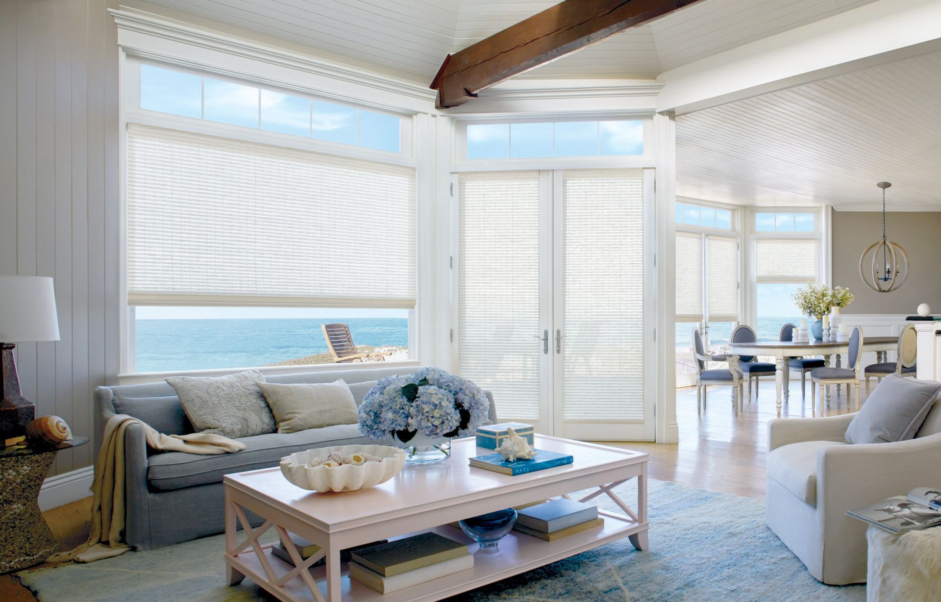 Living room with ocean view, gray sofa, white walls, and sheer window coverings.