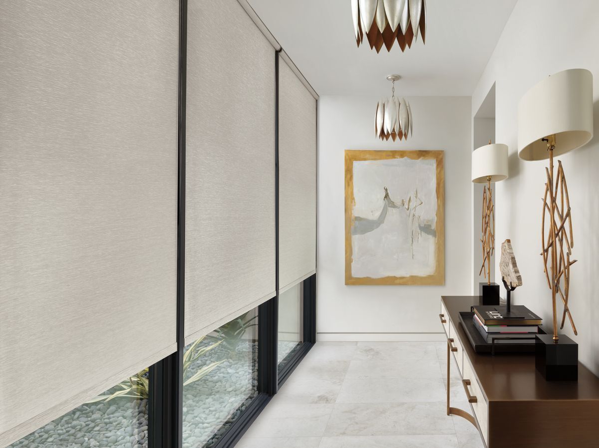 Hallway with beige roller shades, dark trim windows, artwork, and console table.