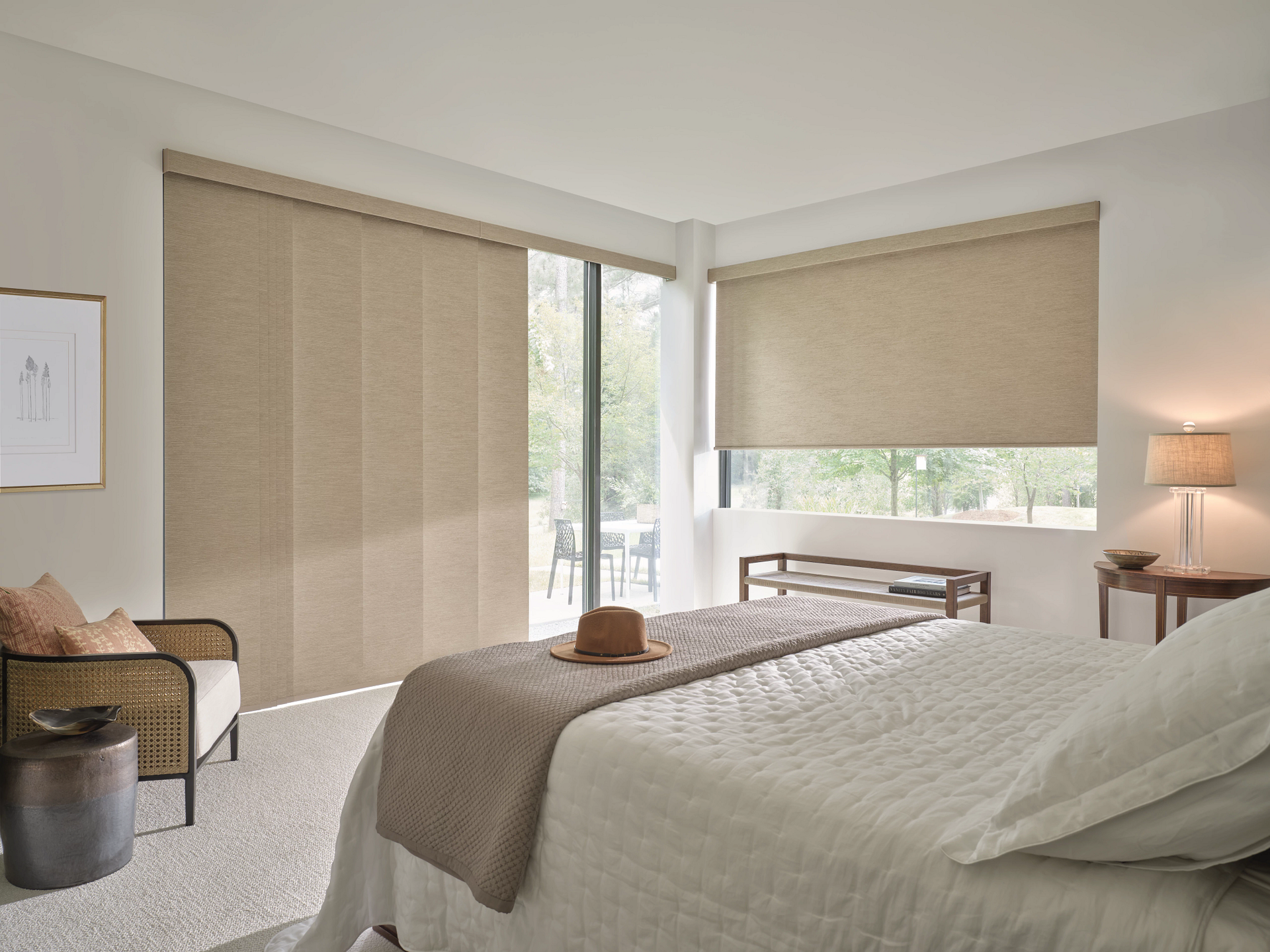 Bedroom with neutral-colored window blinds, bed, chair, and side table with lamp.