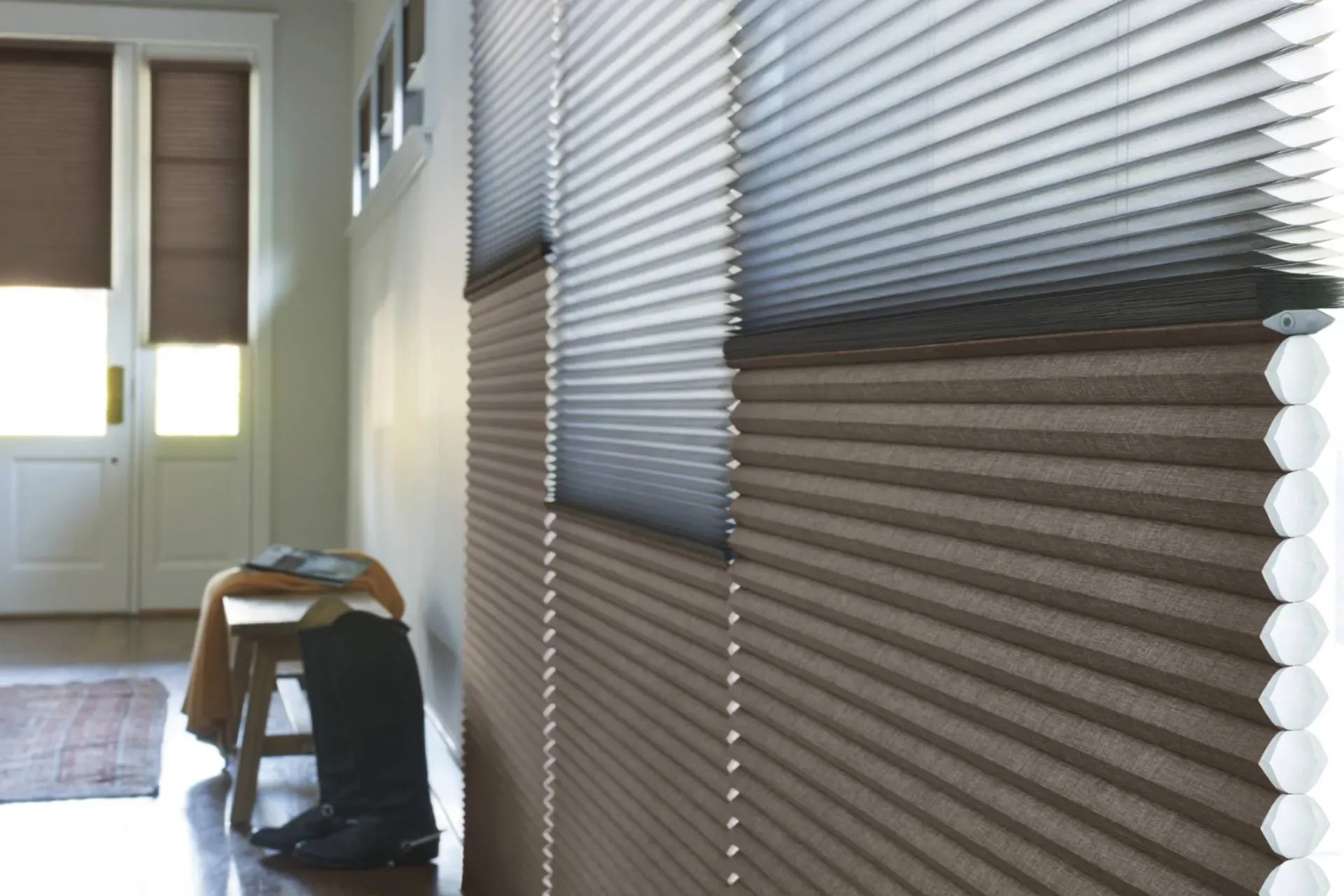 Brown pleated cellular shades partially covering a wall, with a door and bench in the background.