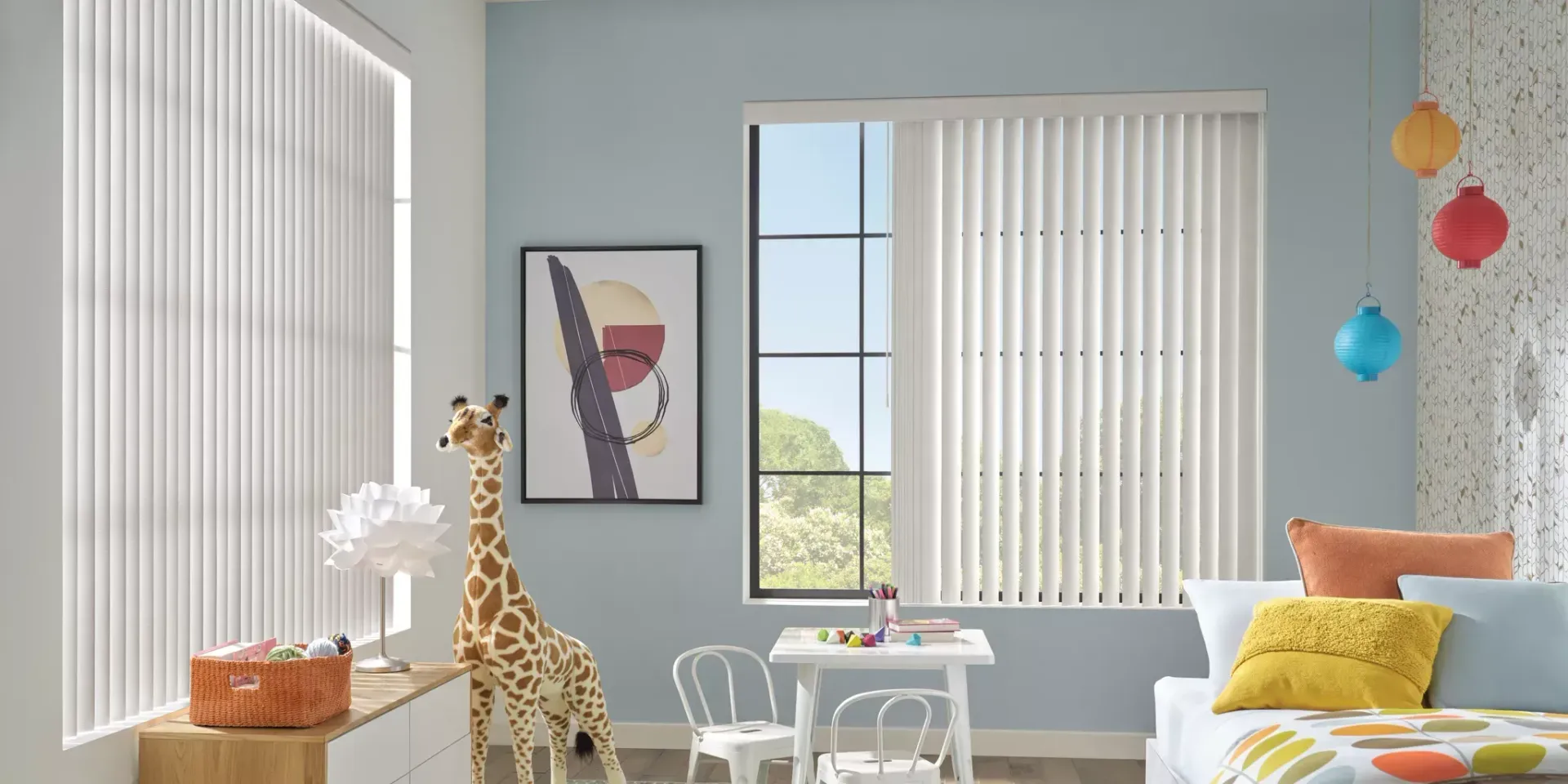 Child's bedroom with blue walls, white blinds, a giraffe, artwork, and a small table.