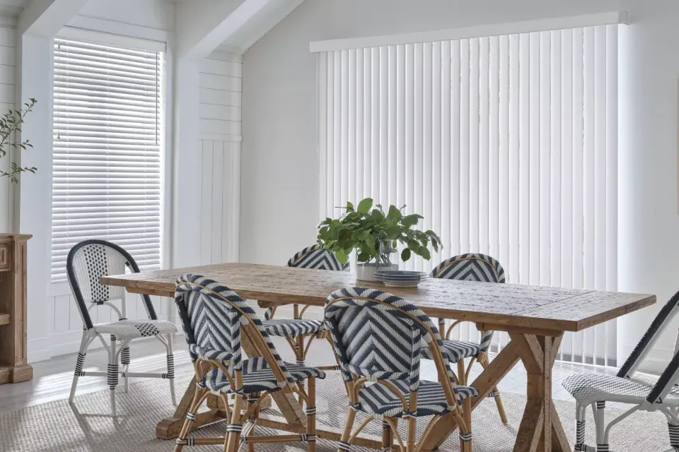 Dining room with wooden table, patterned chairs, and white blinds.