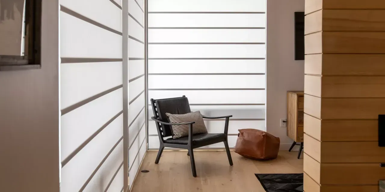 A modern living room with a black armchair, window blinds, and wood paneling.