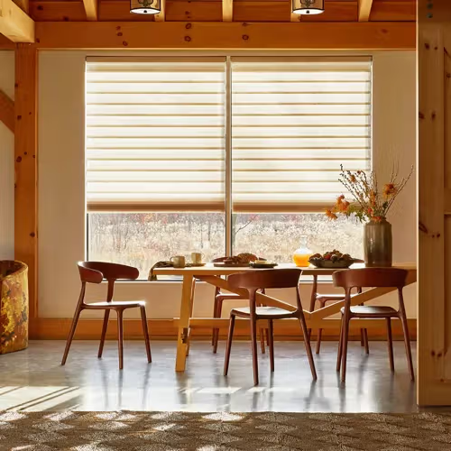 Dining room with wooden table and chairs, window with blinds, vase of flowers.