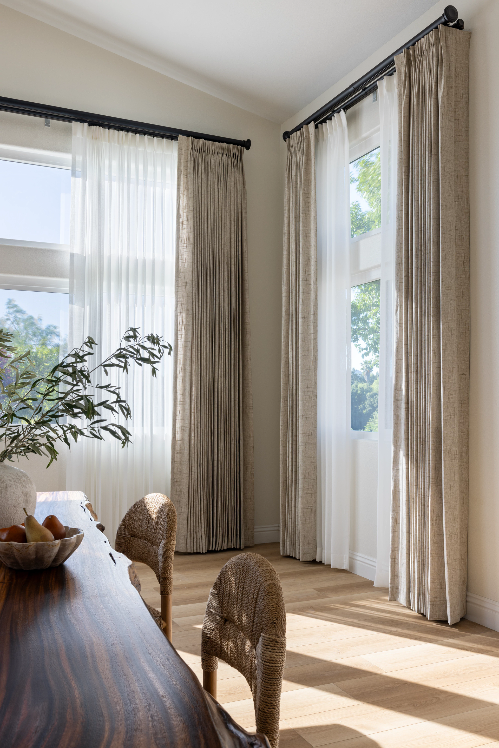 Dining room with sheer white and patterned beige curtains, wooden table, and woven chairs.