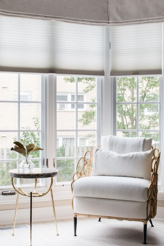 Corner window with light-colored blinds, chair with decorative gold frame, small table, and foliage.