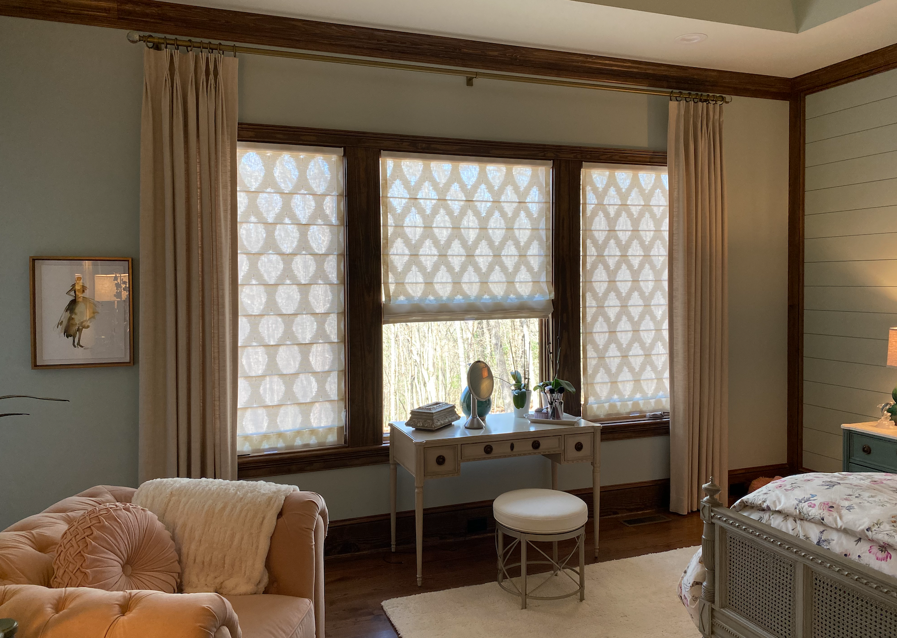 Bedroom with vanity under window, light curtains and patterned shades. Blue walls, wood trim, and a sofa.