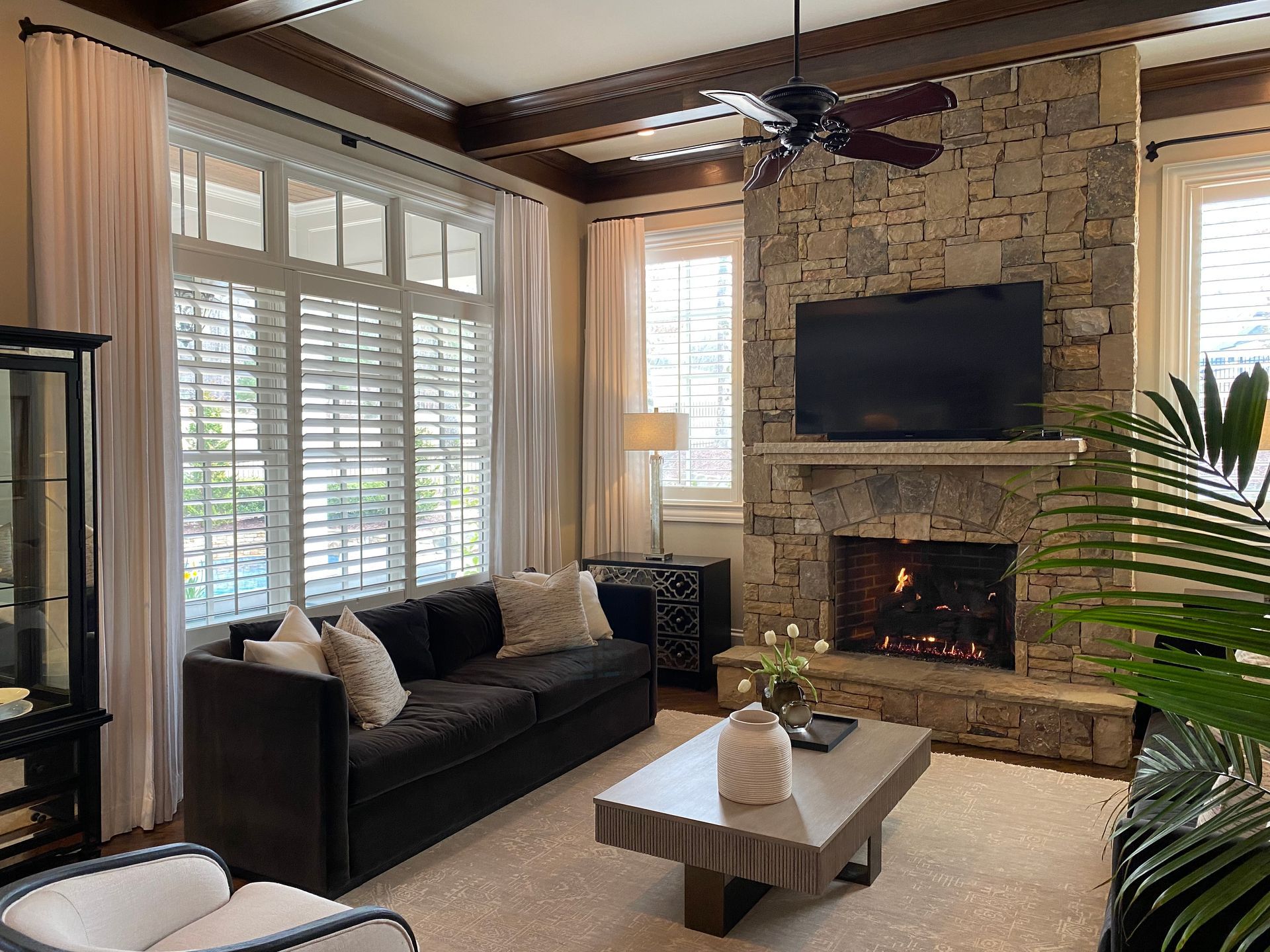 Living room with a stone fireplace, dark sofa, and large windows.
