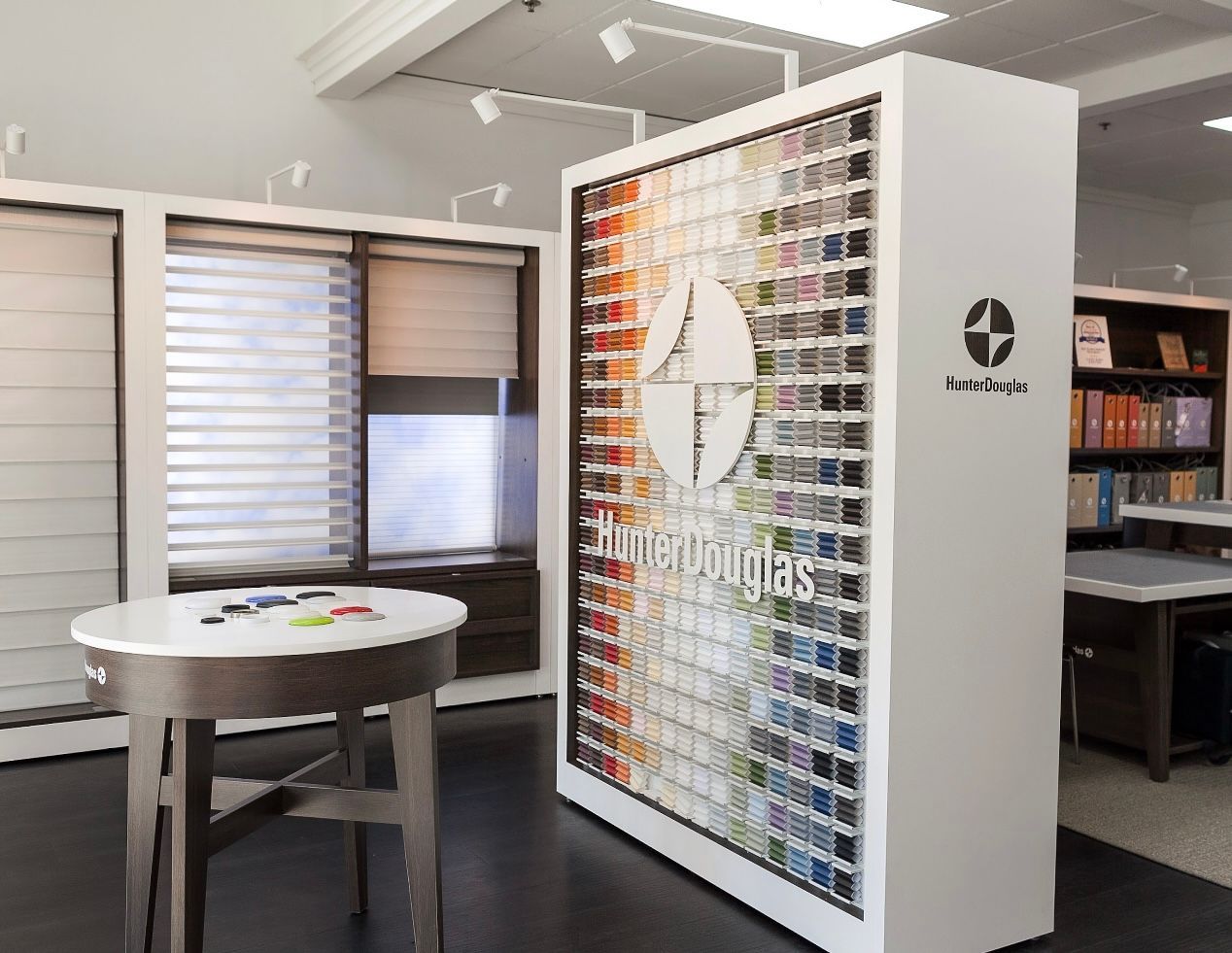 A showroom display of window coverings with a large color sample panel, a table, and blinds.