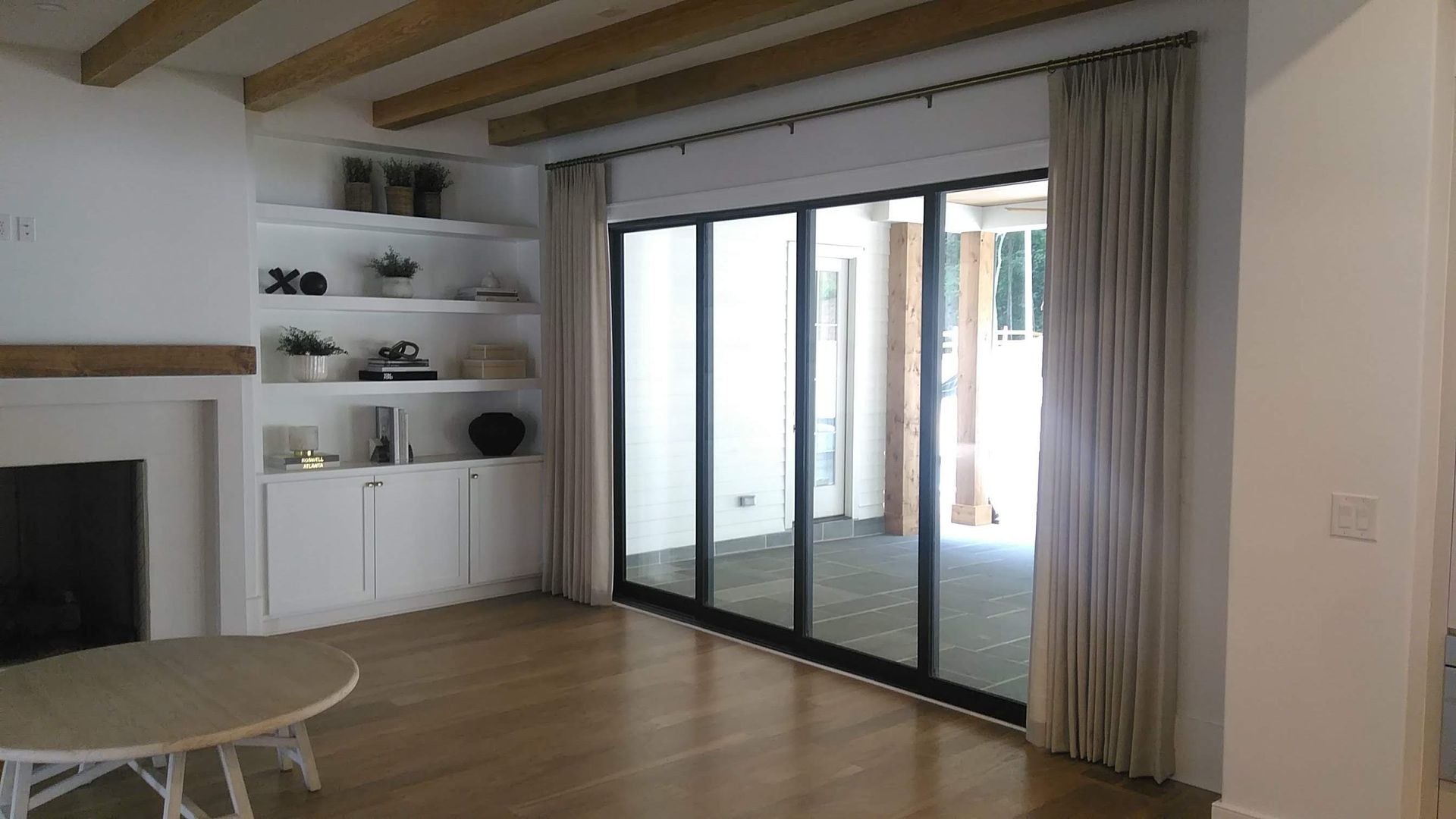 Living room with built-in shelves, fireplace, and sliding glass doors with beige curtains.