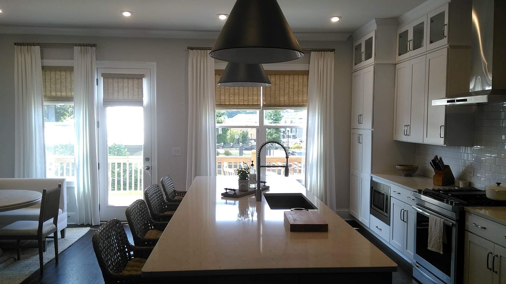 Kitchen with island, windows, white cabinets, and dark floor. Three black pendant lights hang above the island.