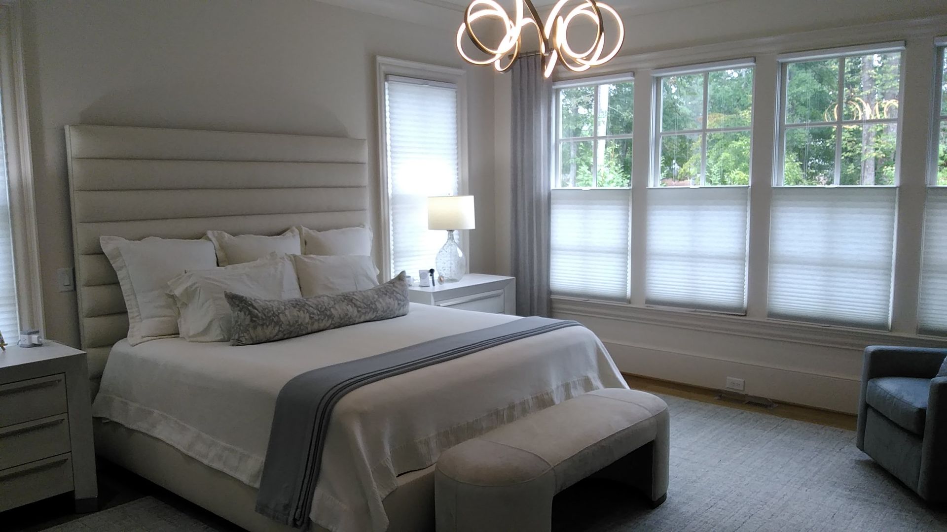 Bedroom with bed, windows, neutral colors, and modern chandelier.