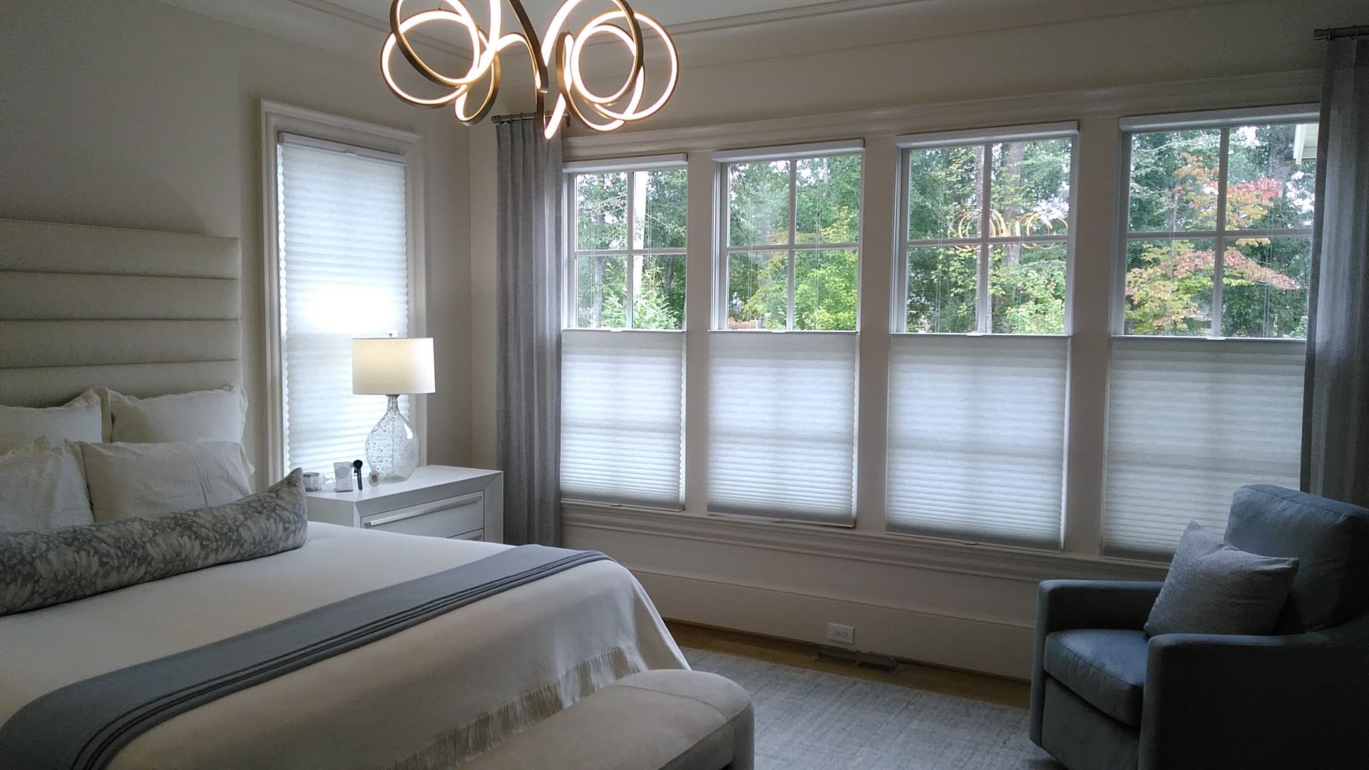 Bedroom with bed, windows, armchair, and modern chandelier. Neutral color scheme.
