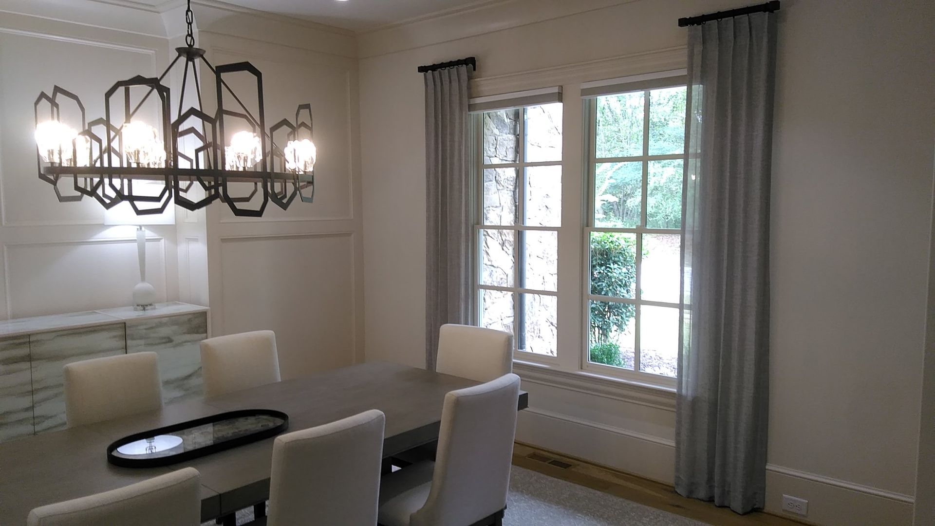 Dining room with a chandelier, table, chairs, and light blue curtains.