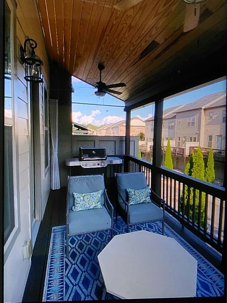 Covered patio with blue chairs, rug, and grill. Wooden ceiling and view of neighborhood.