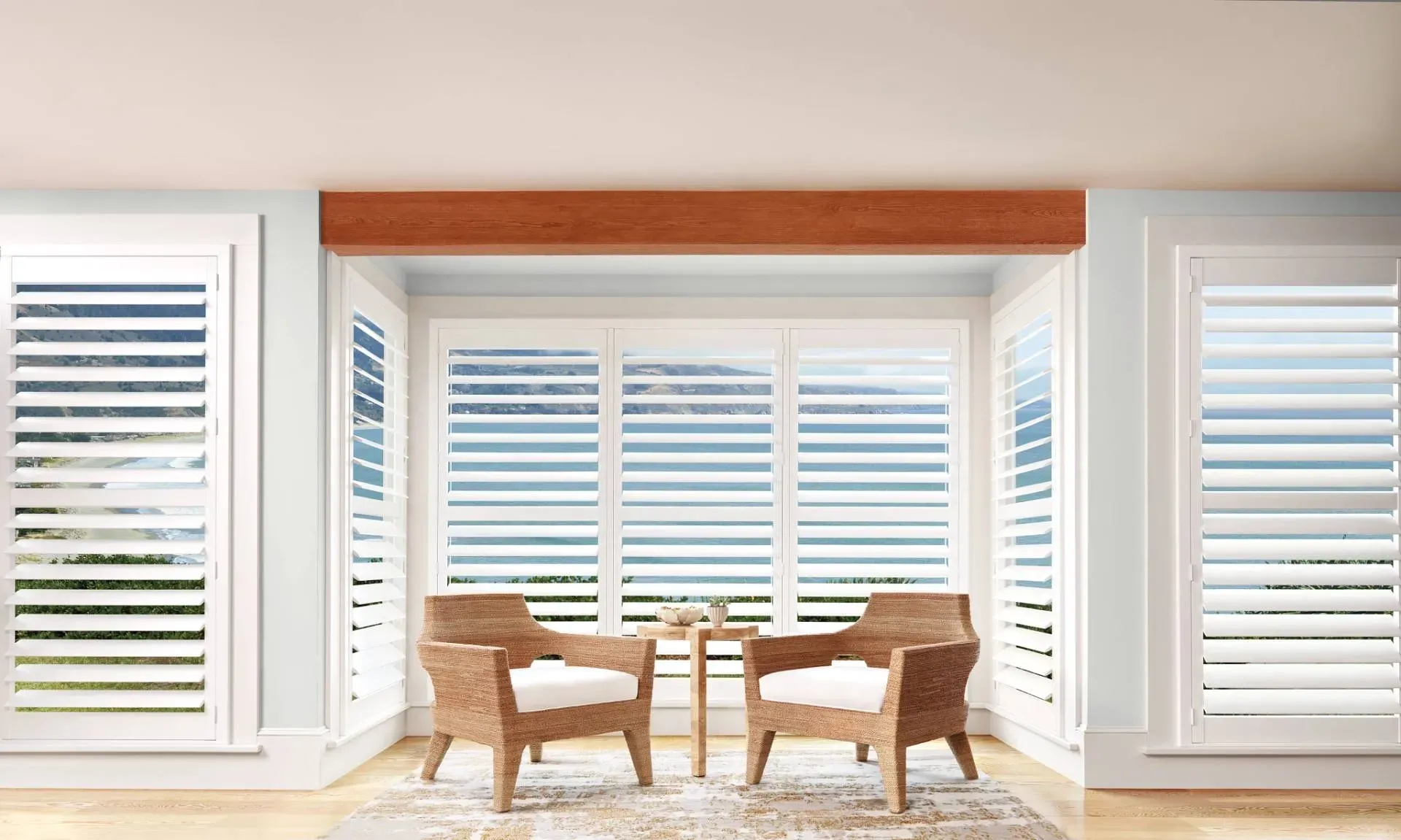 Two wicker chairs facing each other in front of a window with white shutters, beneath a wood beam.