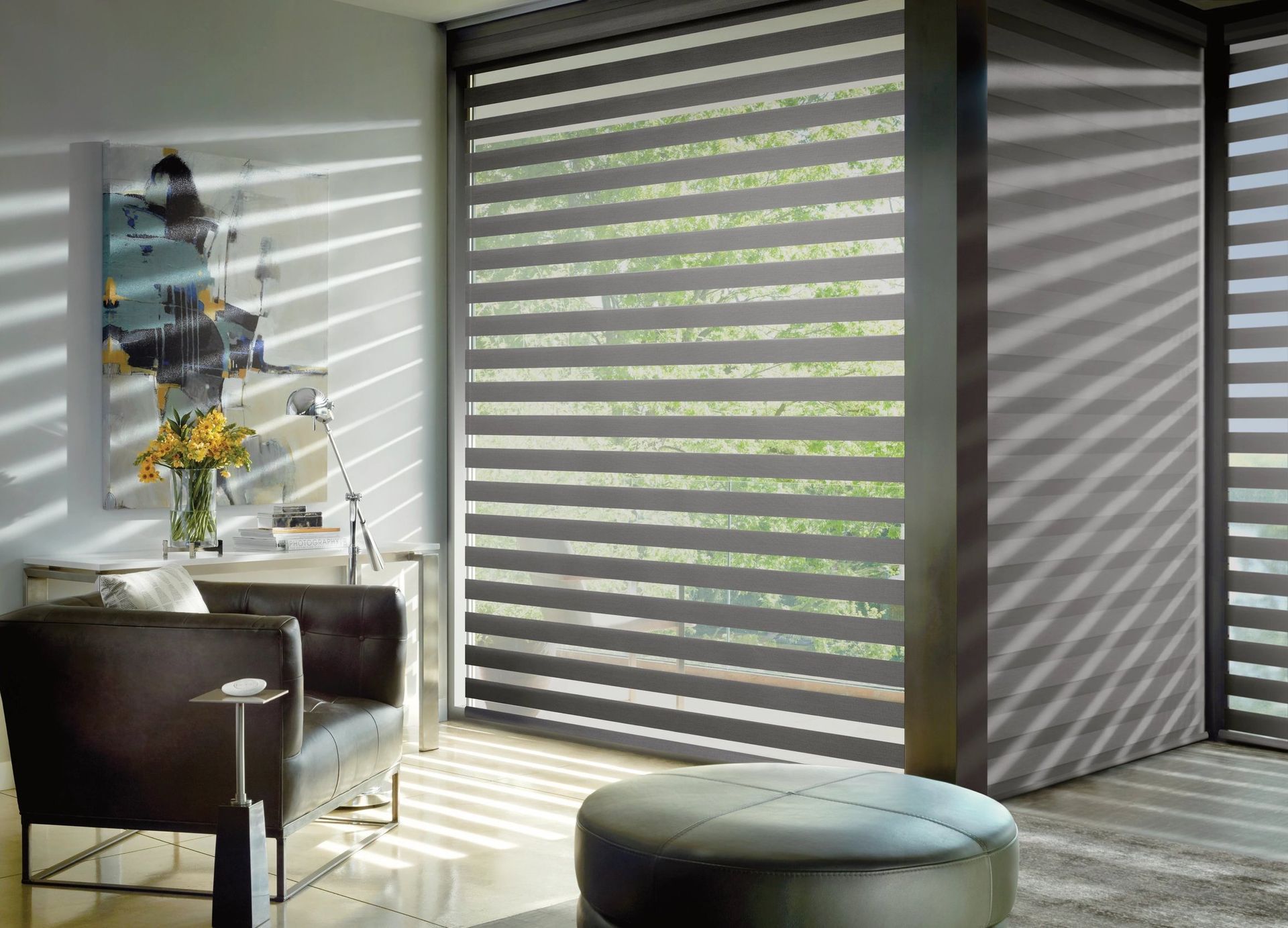 Interior with modern blinds casting striped shadows; chair, art, and ottoman.