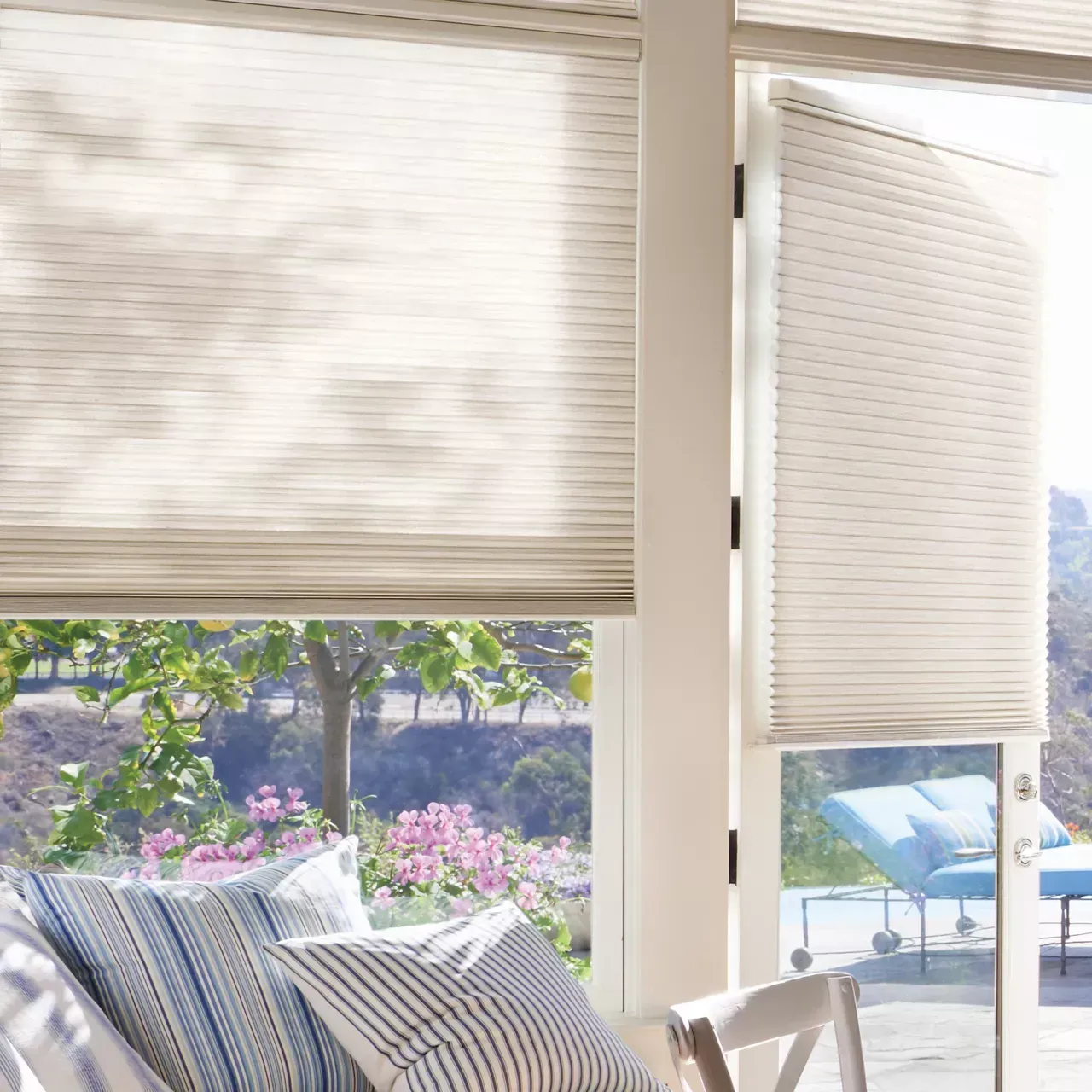Beige pleated blinds partially cover a glass door, overlooking a patio and garden.