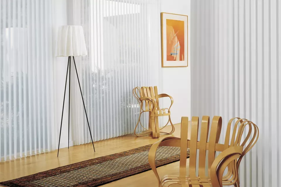 Room with wooden floor, striped wall, two chairs, a lamp, and artwork.