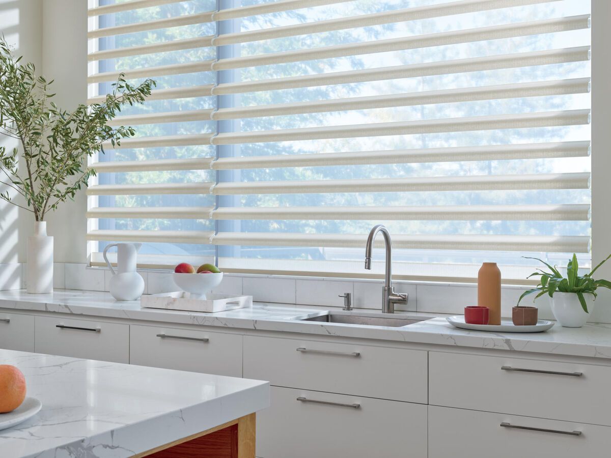 Kitchen with horizontal striped blinds, white cabinets, and countertop with decor.