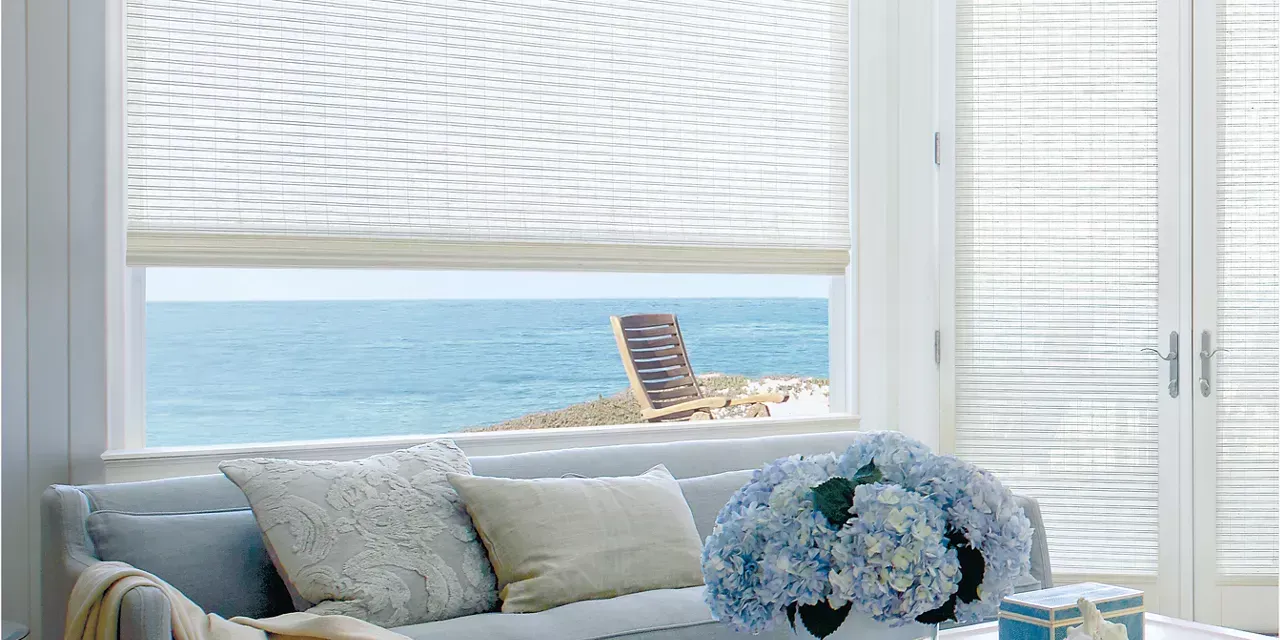 Living room with ocean view, white blinds, blue sofa with pillows, and hydrangea bouquet.