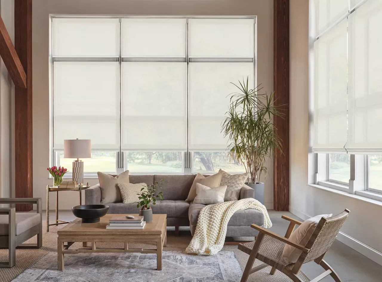 Living room with neutral-toned furniture and large windows covered by light-colored shades.