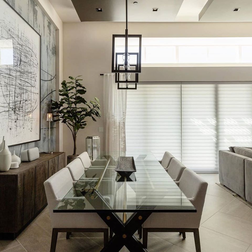 Elegant dining room with glass table, chairs, art, cabinet, and pendant light.