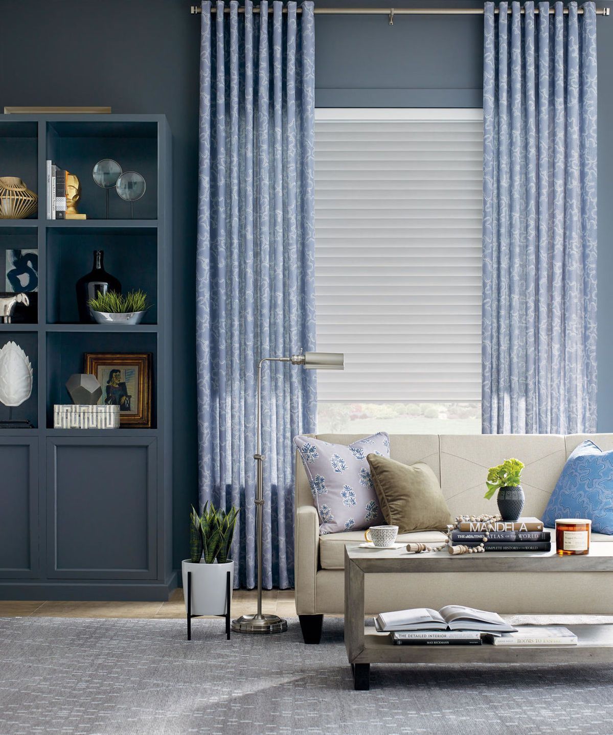 Blue living room with bookshelf, couch, patterned curtains, and a coffee table.