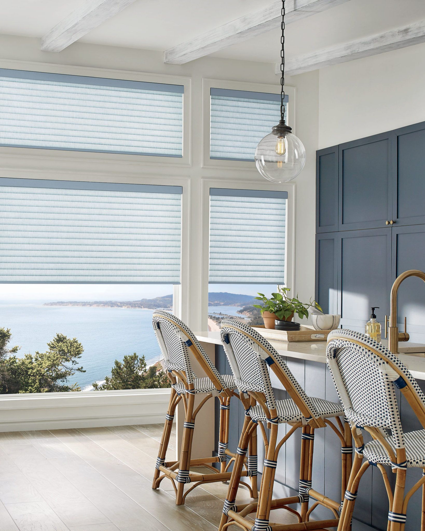 Kitchen with blue cabinets, sea view, and rattan bar stools. Light blue shades.