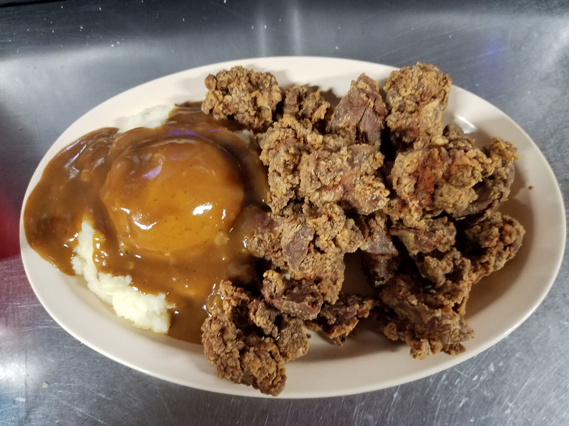 A serving of fried chicken gizzards next to a scoop of mashed potatoes topped with brown gravy on an oval plate.
