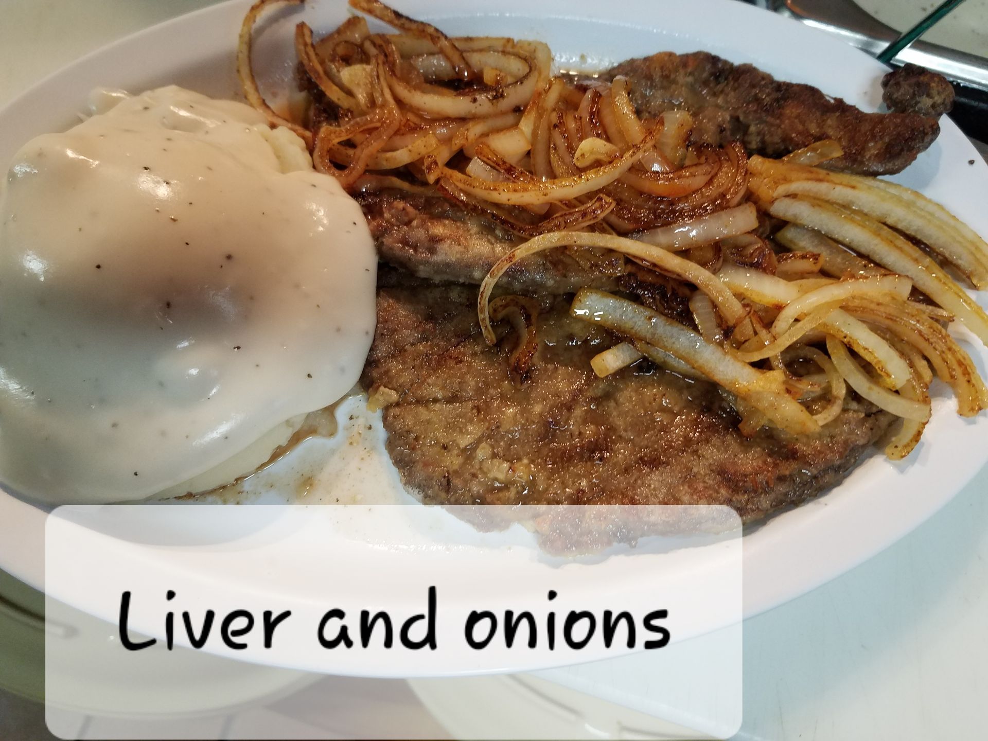 A plate featuring pan-fried liver topped with sautéed onions, served alongside a mound of mashed potatoes with gravy.