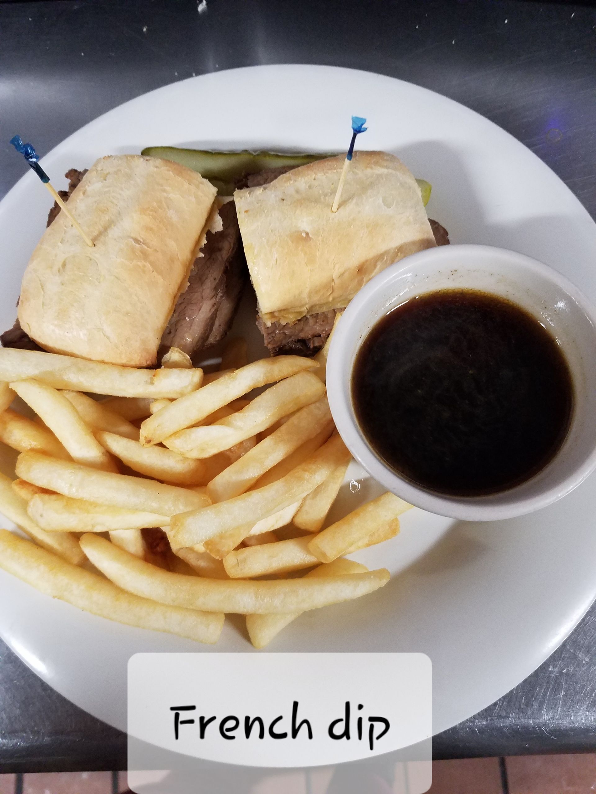 A French dip sandwich on a plate with golden fries and a side of dark au jus dipping sauce.